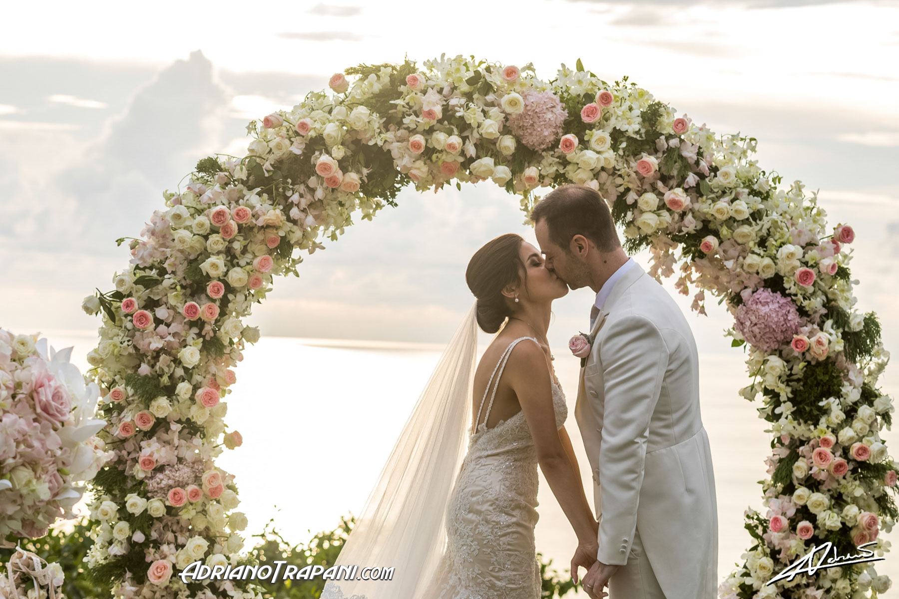 Wedding photography bride and groom kiss by the flower arch.